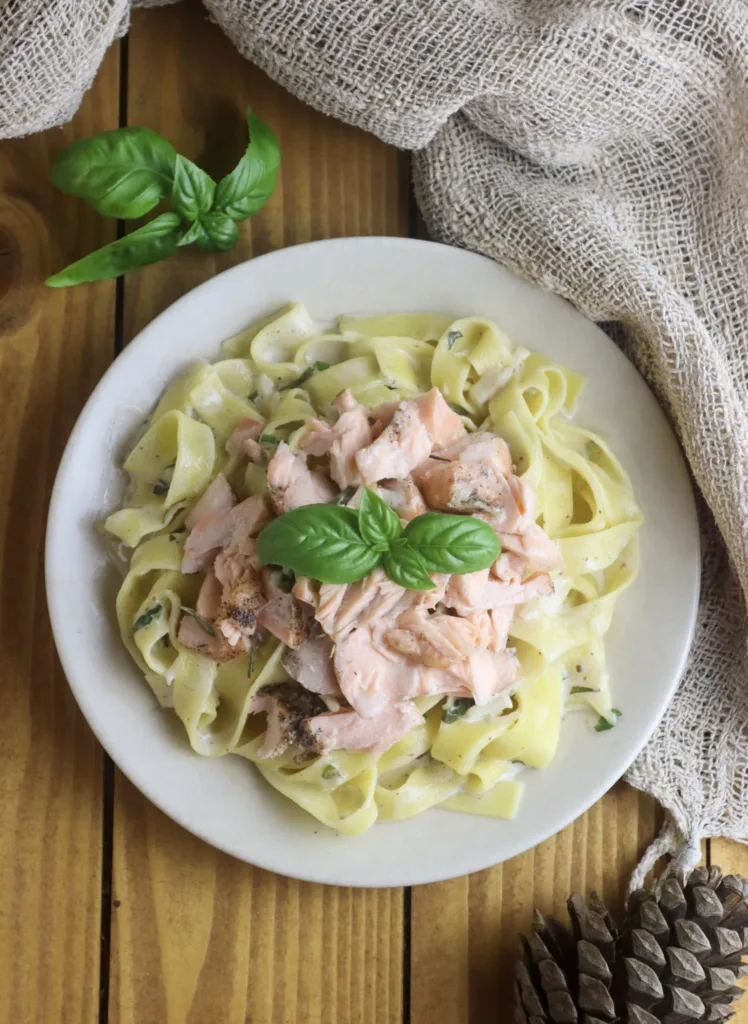 placing pasta and salmone with the sauce to the plate with basil decoration